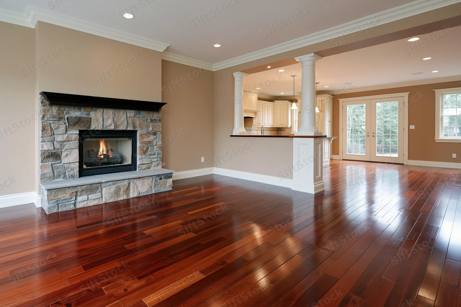 Empty luxury living room with dark cherry hardwood floor and stone fireplace adjacent to kitchen bar with white columns