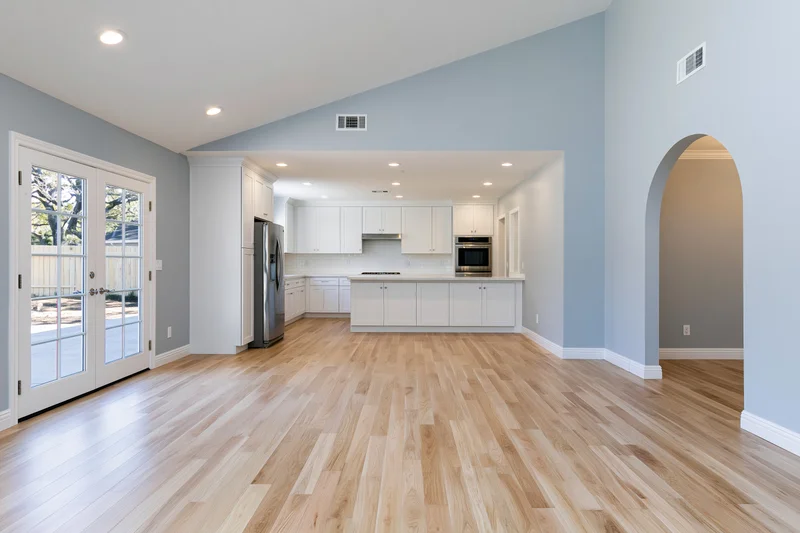 Empty open-plan kitchen and living area with hardwood flooring and white cabinetry in a residential home