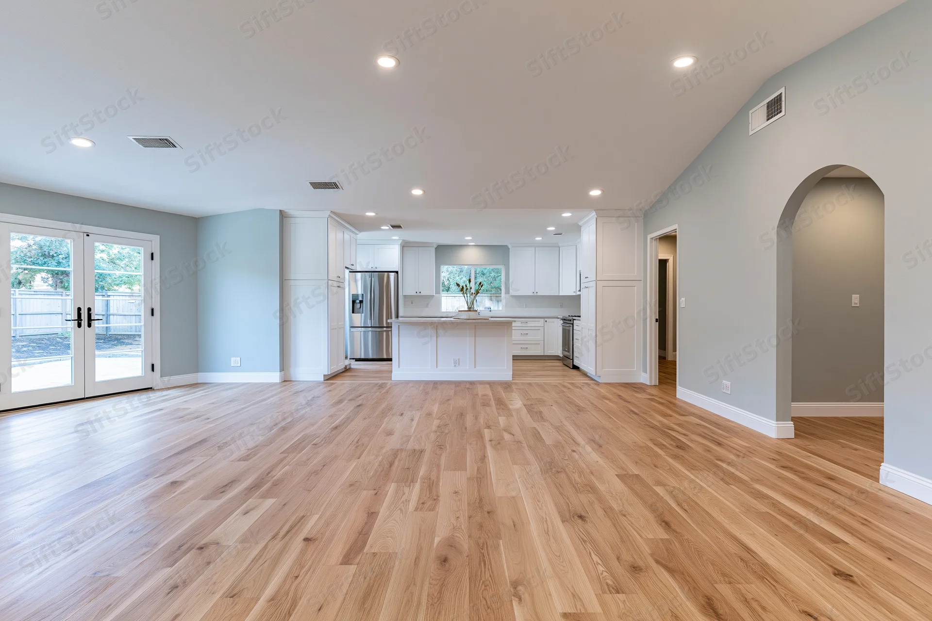 Empty open-plan kitchen and living area with hardwood flooring and white cabinetry in a residential home