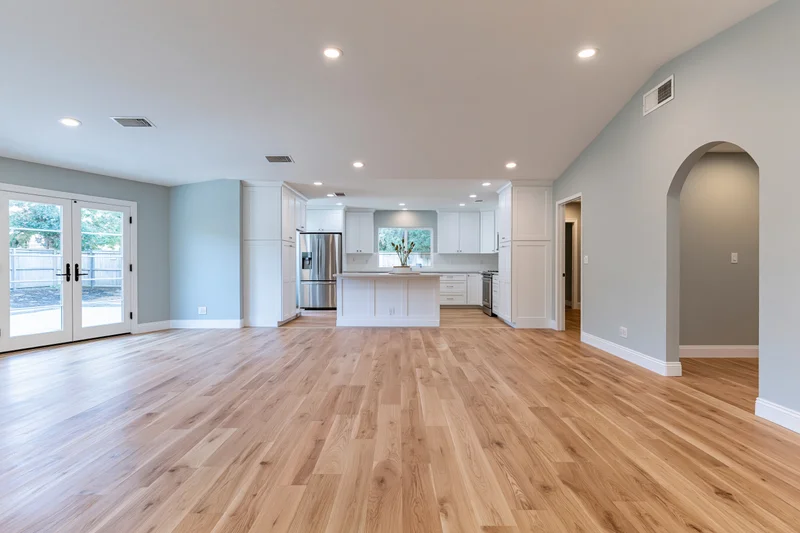 Empty open-plan kitchen and living area with hardwood flooring and white cabinetry in a residential home