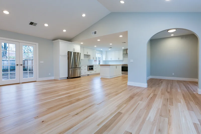 Empty open-plan kitchen and living area with hardwood flooring and white cabinetry in a residential home