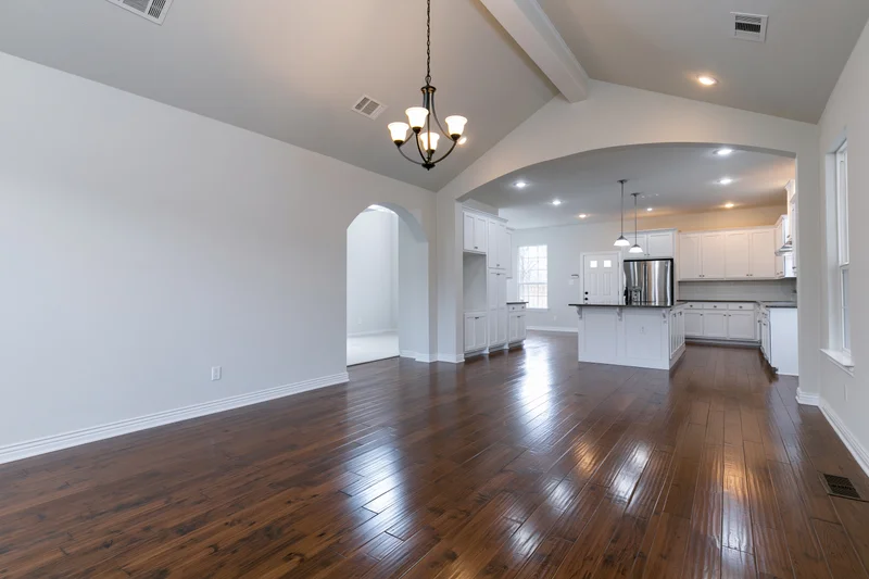 Empty open-plan living and kitchen area with hardwood floors and white cabinetry in a newly built home