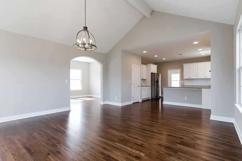 Empty open-plan living and kitchen area with hardwood floors and white cabinetry in a newly built home
