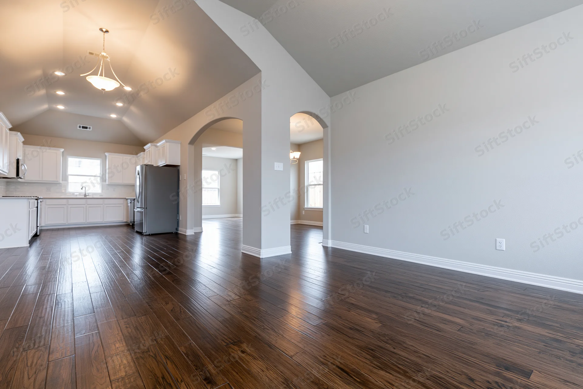 Empty open-plan living and kitchen area with hardwood floors and vaulted ceiling in a newly built home