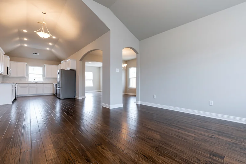Empty open-plan living and kitchen area with hardwood floors and vaulted ceiling in a newly built home