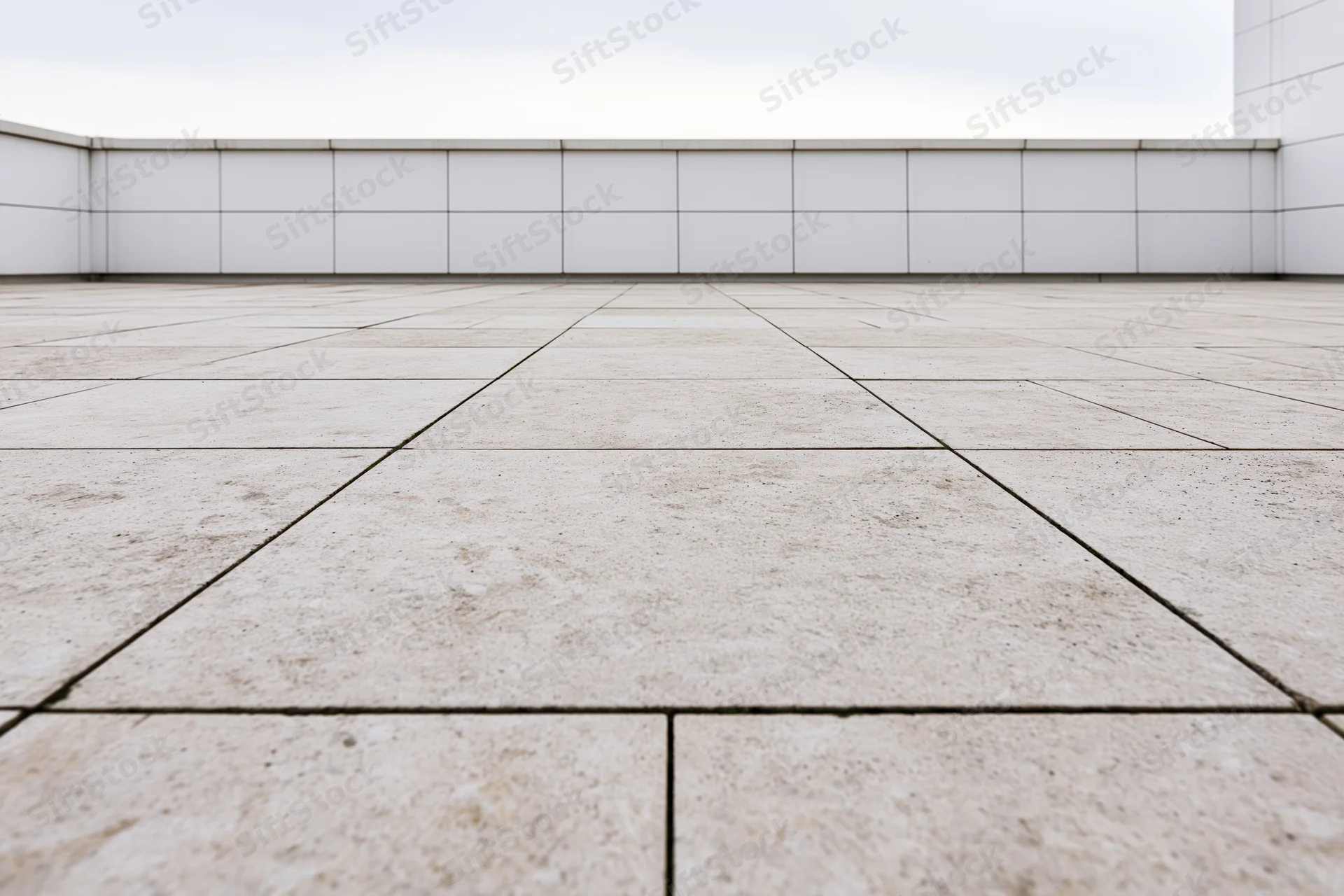 Empty outdoor plaza with large beige concrete paving slabs arranged in a grid pattern against white tiled walls