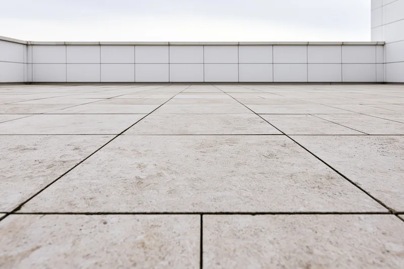 Empty outdoor plaza with large beige concrete paving slabs arranged in a grid pattern against white tiled walls
