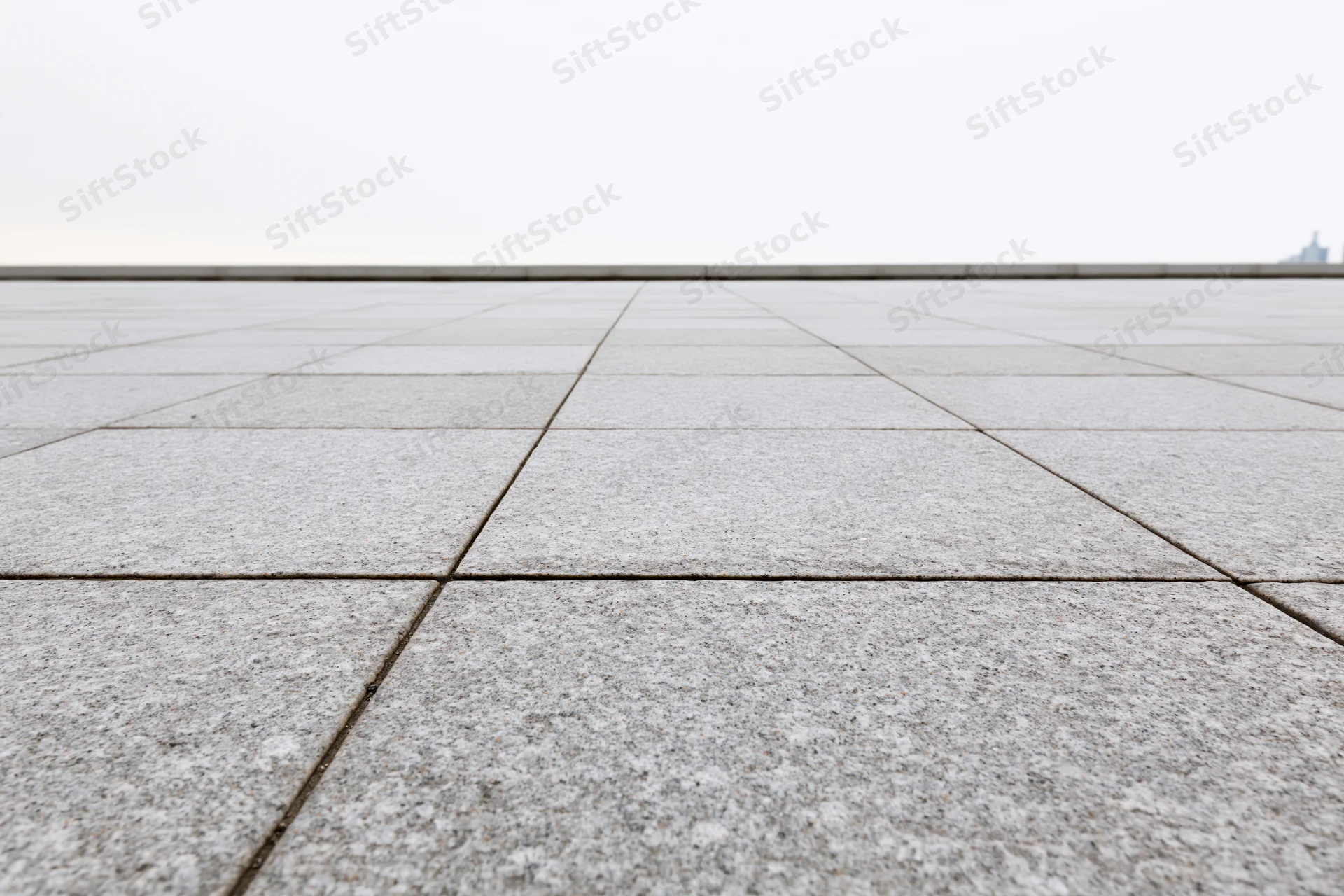 Stone tile plaza floor receding into the distance under overcast sky