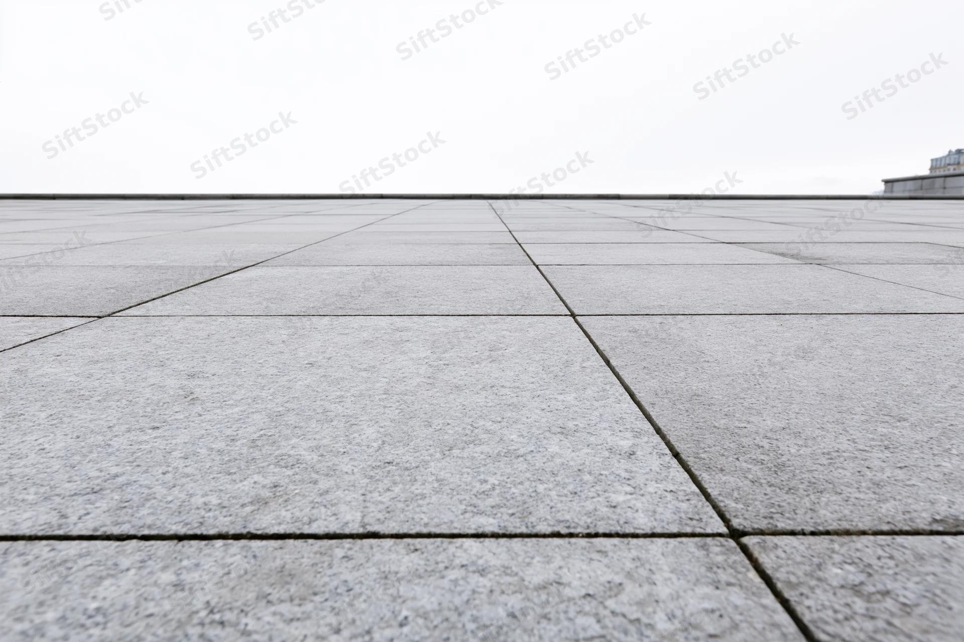 Stone tile plaza floor receding into the distance under overcast sky
