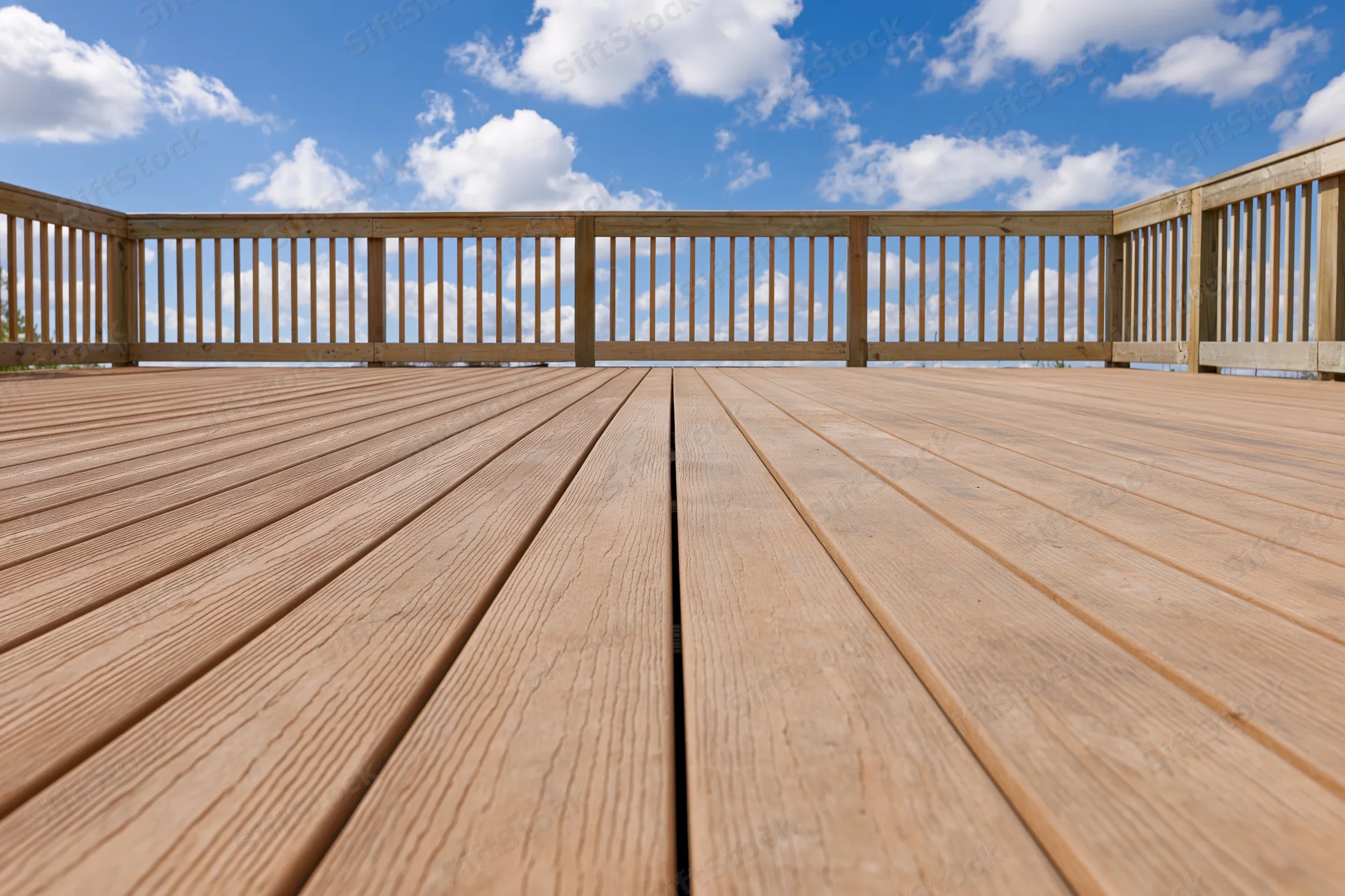 Wooden deck with horizontal planks and railing under blue sky with clouds