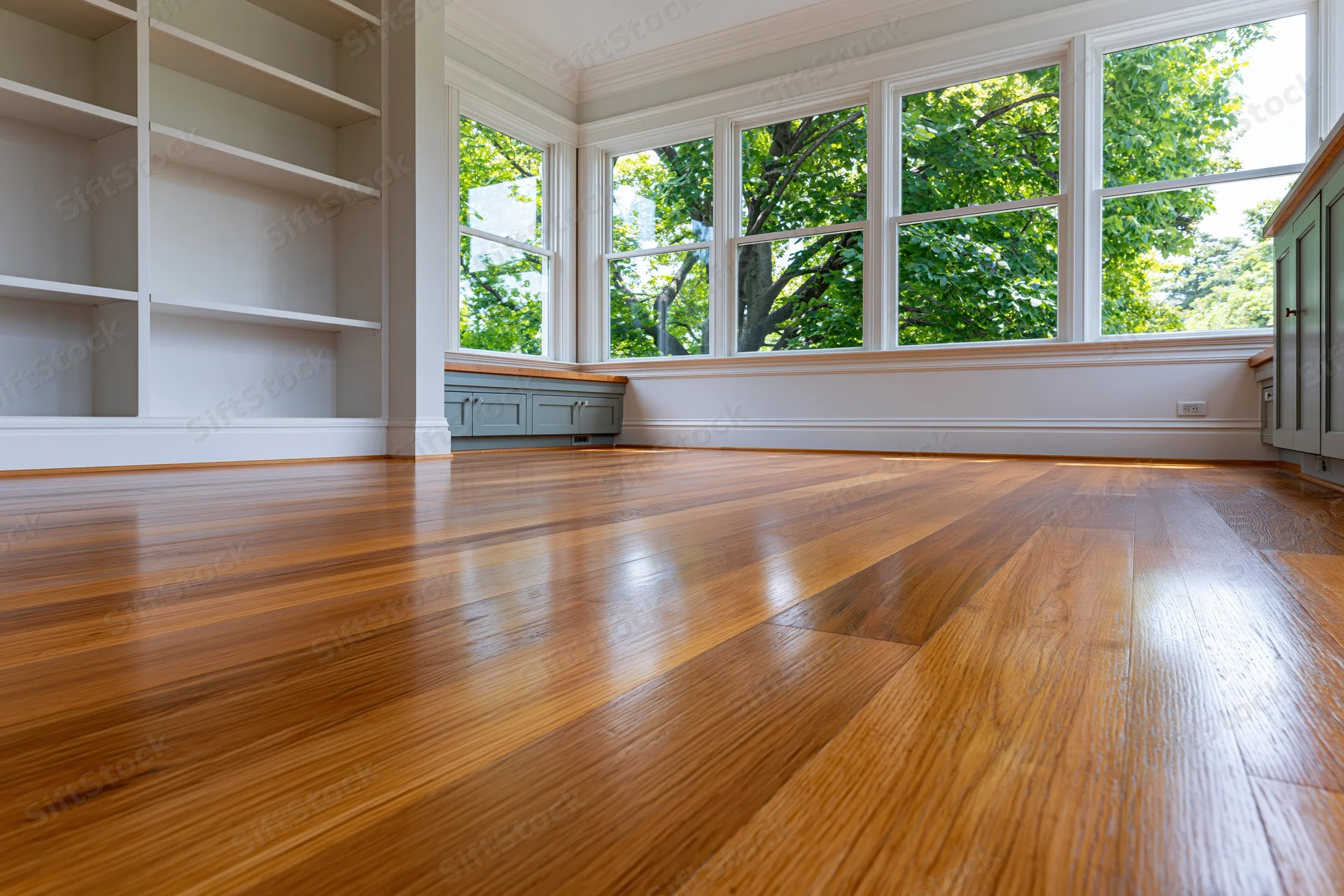 Empty residential room with refinished hardwood floor and built-in shelves near large windows
