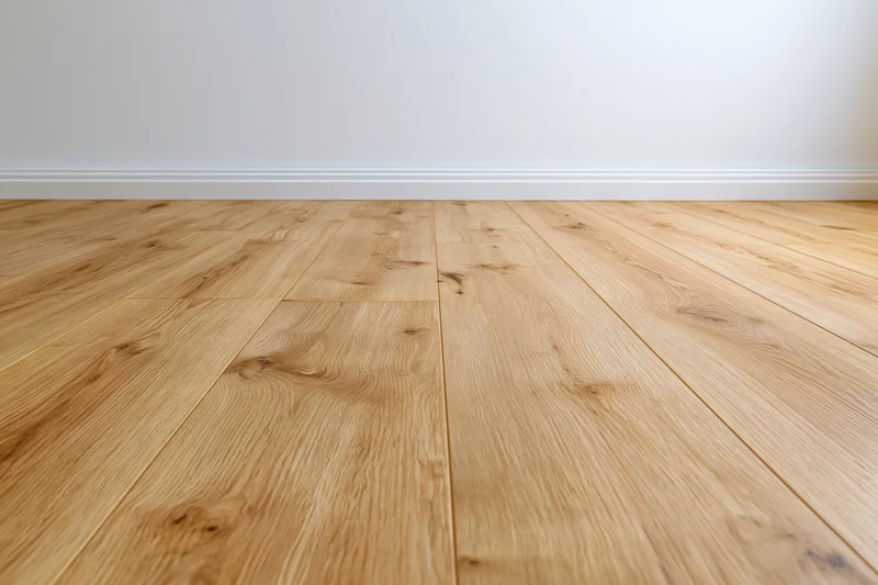 Light oak wood laminate flooring in an empty room interior with white walls and baseboard trim