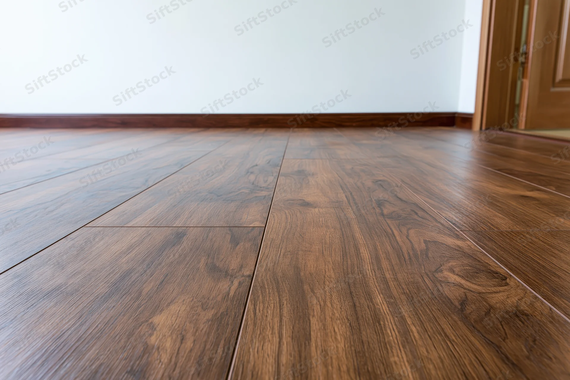Dark walnut laminate flooring in an empty room interior with baseboard and door trim
