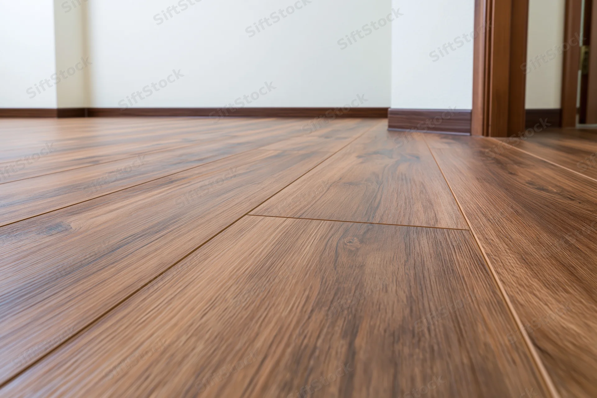 Dark walnut laminate flooring in an empty room interior with baseboards and doorframe