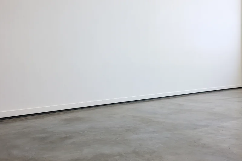 Plain white wall meeting gray concrete floor in empty room interior