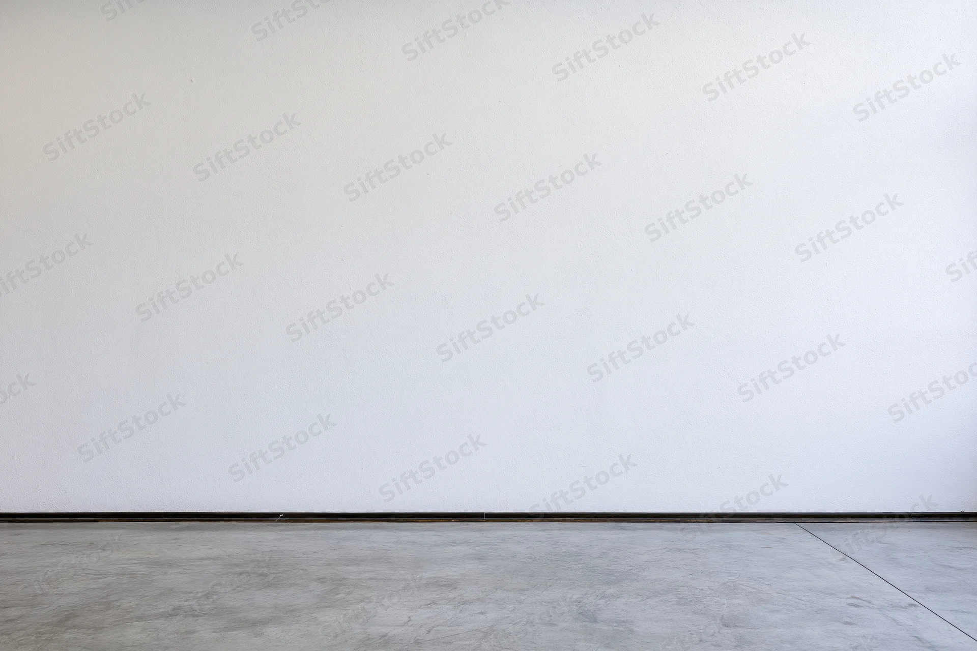 Empty room interior with bare white plaster wall meeting concrete floor at baseboard