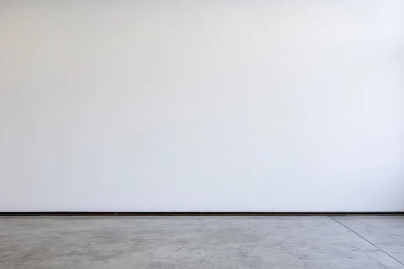 Empty room interior with bare white plaster wall meeting concrete floor at baseboard