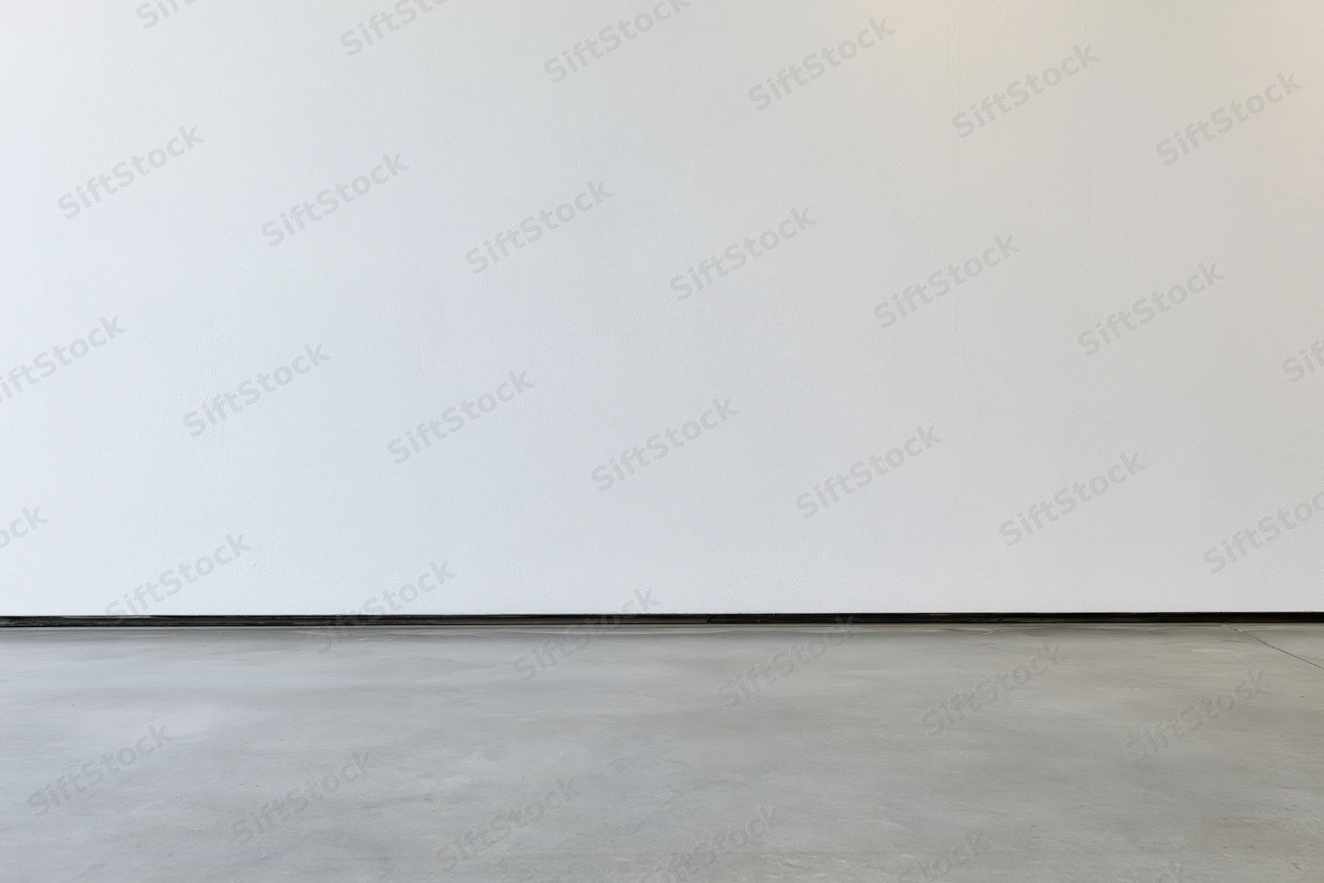 Empty room interior with bare white plaster wall meeting smooth concrete floor
