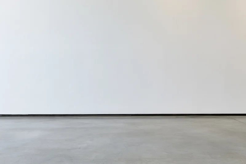 Empty room interior with bare white plaster wall meeting smooth concrete floor