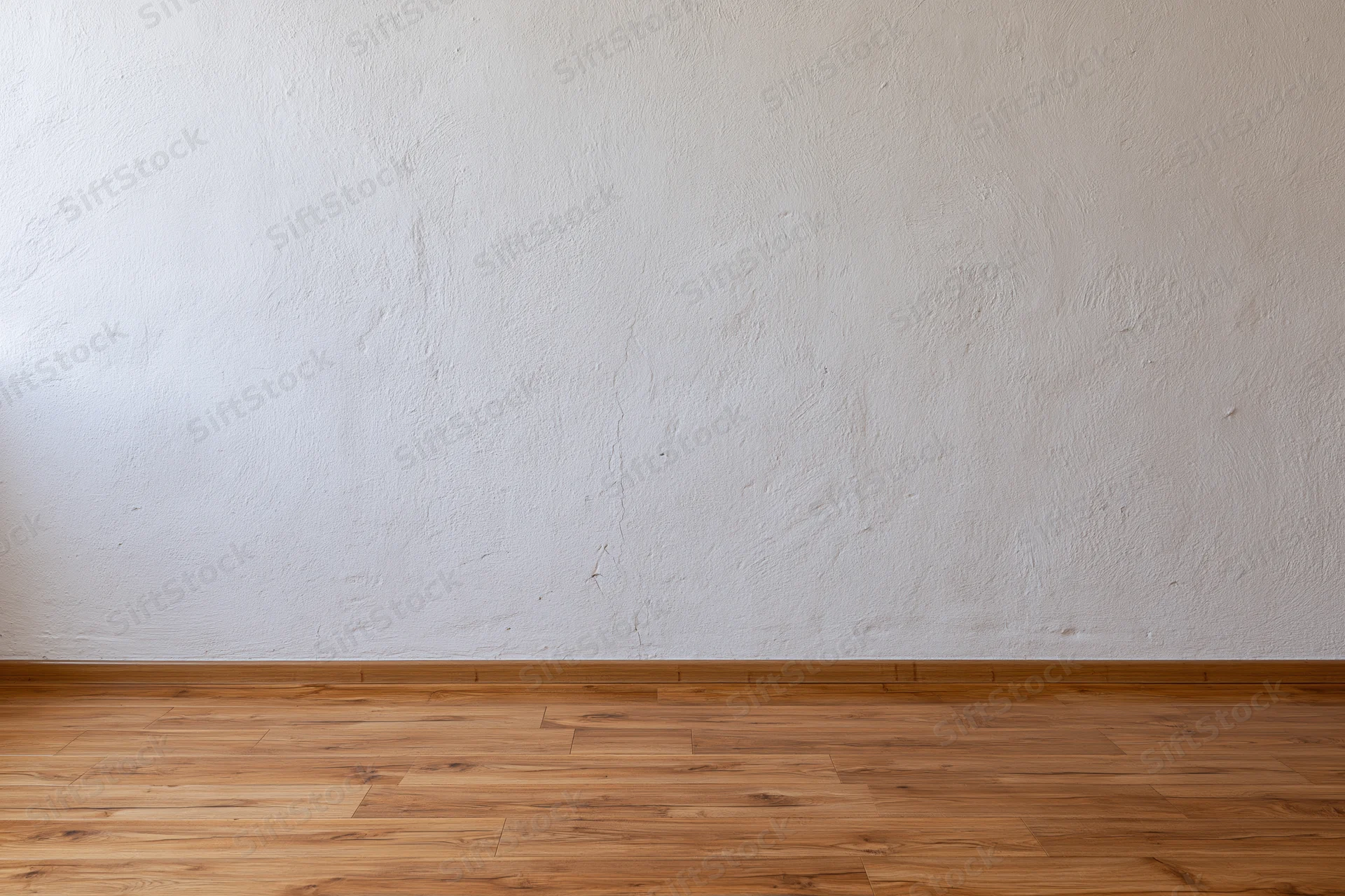 Empty room interior with textured white plaster wall meeting light wood laminate floor at baseboard