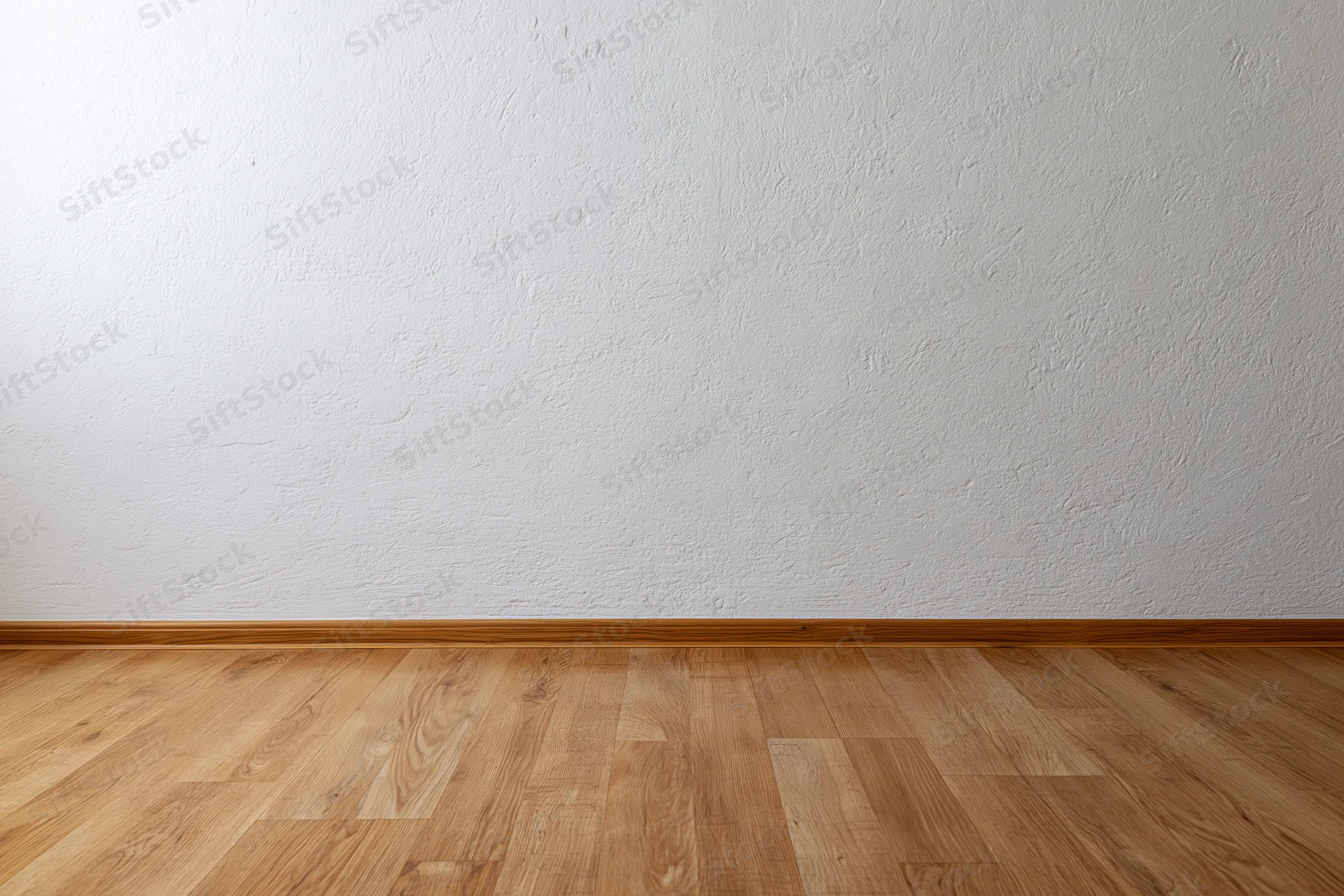 Empty room interior with textured white plaster wall meeting light wood laminate floor at baseboard trim