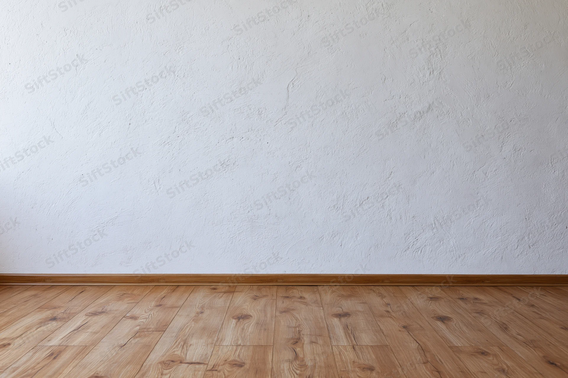 Empty room interior with textured white plaster wall meeting wooden floor at baseboard