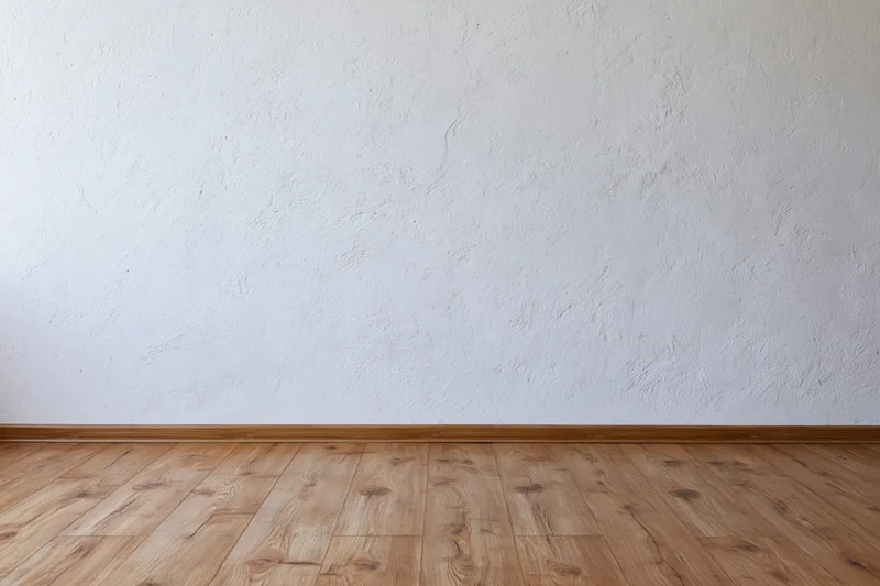 Empty room interior with textured white plaster wall meeting wooden floor at baseboard