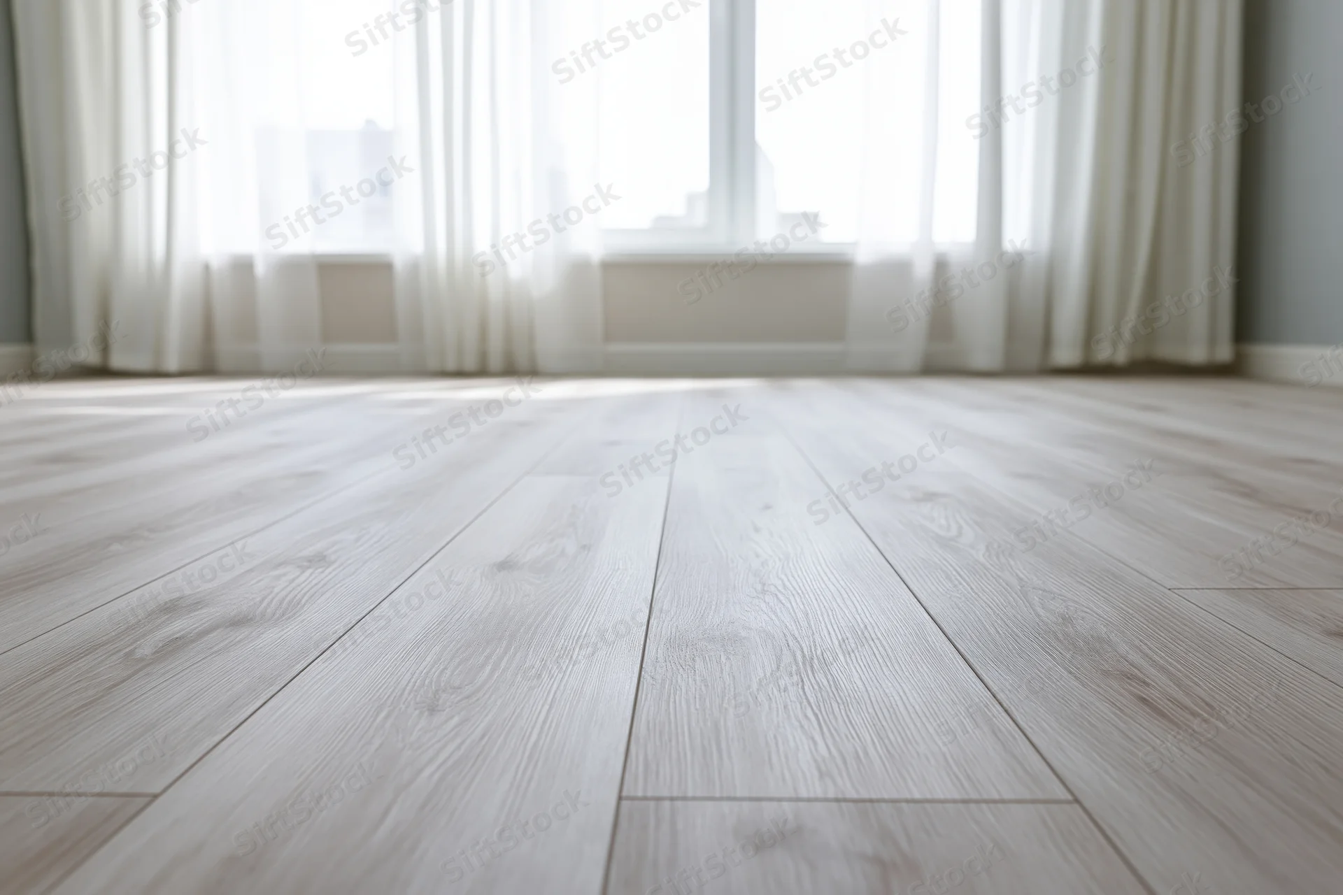 Pale whitewashed hardwood laminate flooring in an empty room with sheer curtains and natural light from a window