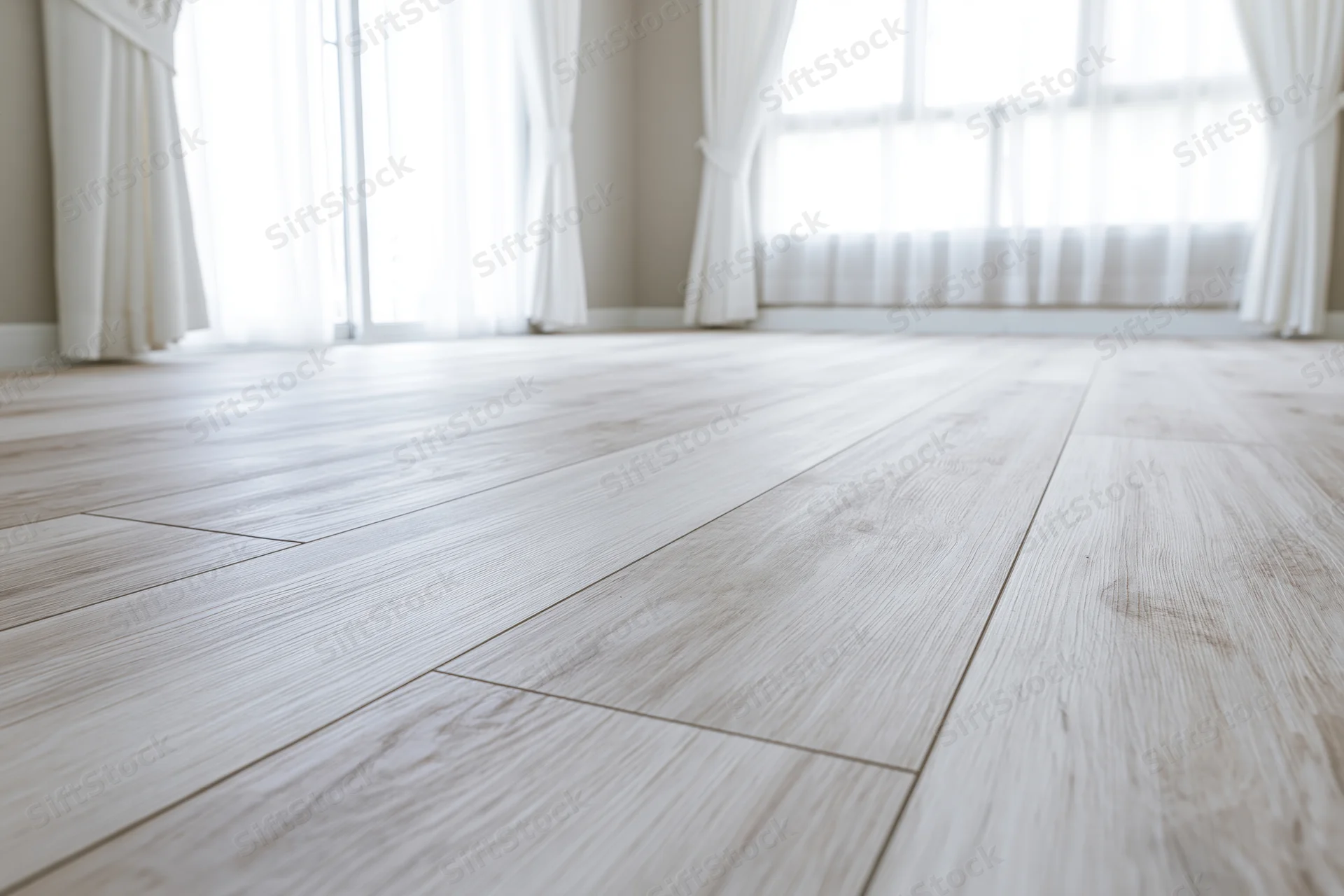 Pale whitewashed hardwood laminate flooring in an empty room with sheer curtains and daylight