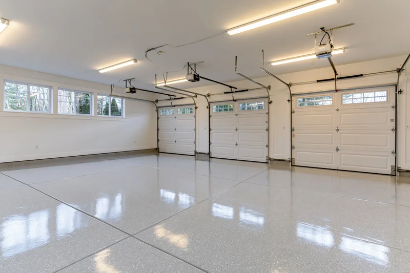 Empty three-car garage interior with white epoxy floor and overhead doors viewed from back wall