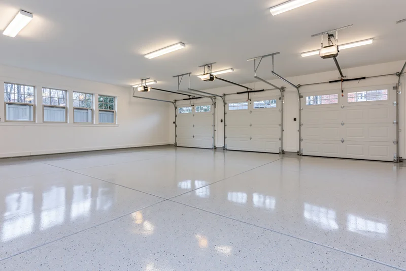 Empty three-car garage interior with white epoxy floor and overhead doors viewed from back wall