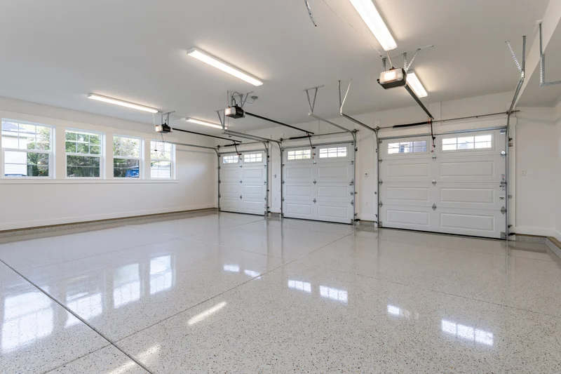 Empty three-car garage interior with white epoxy floor and automatic doors viewed from back wall