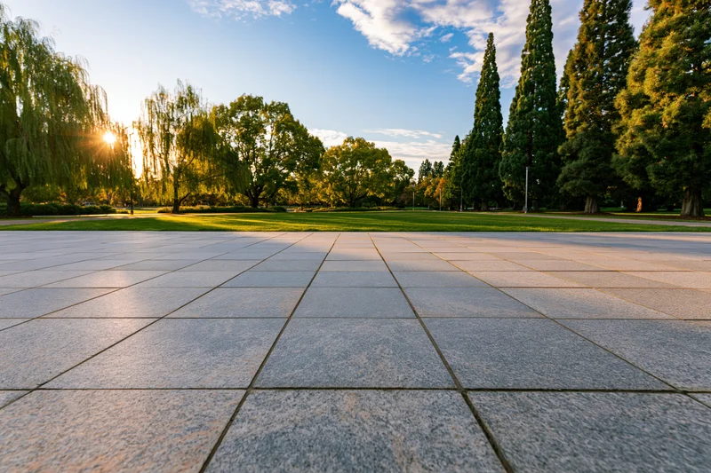 Wide granite tile plaza in front of open green lawn with trees under sunrise sky