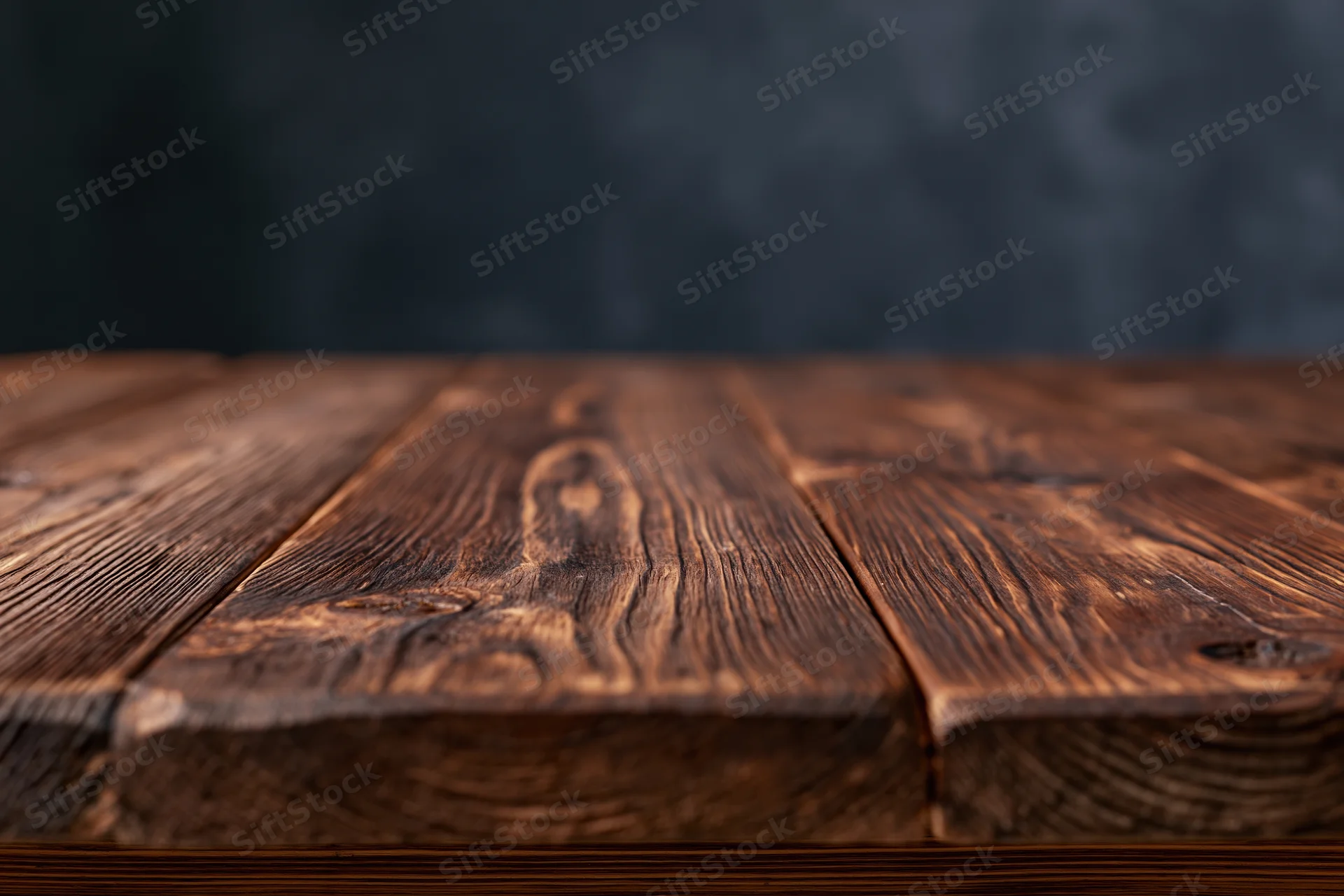 Empty wooden plank tabletop viewed from eye level with dark textured backdrop