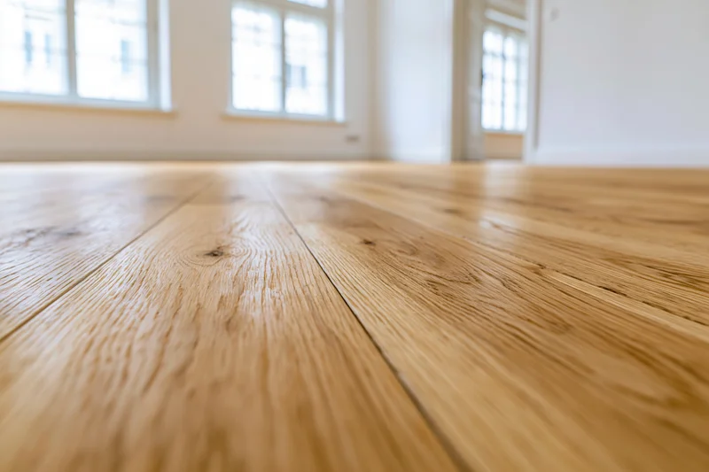 Light oak hardwood flooring planks in a bright interior room with windows in the background