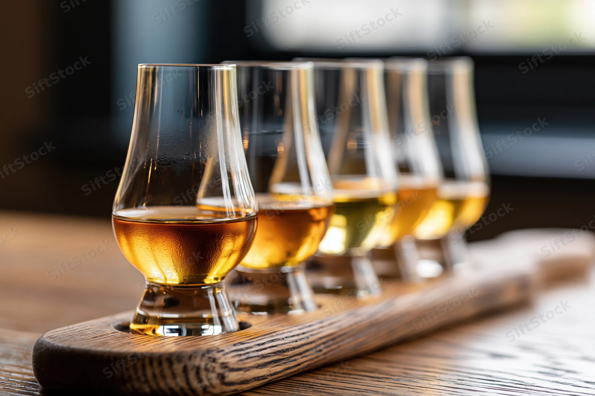 Five glencairn whisky glasses arranged in a wooden flight tray on a table