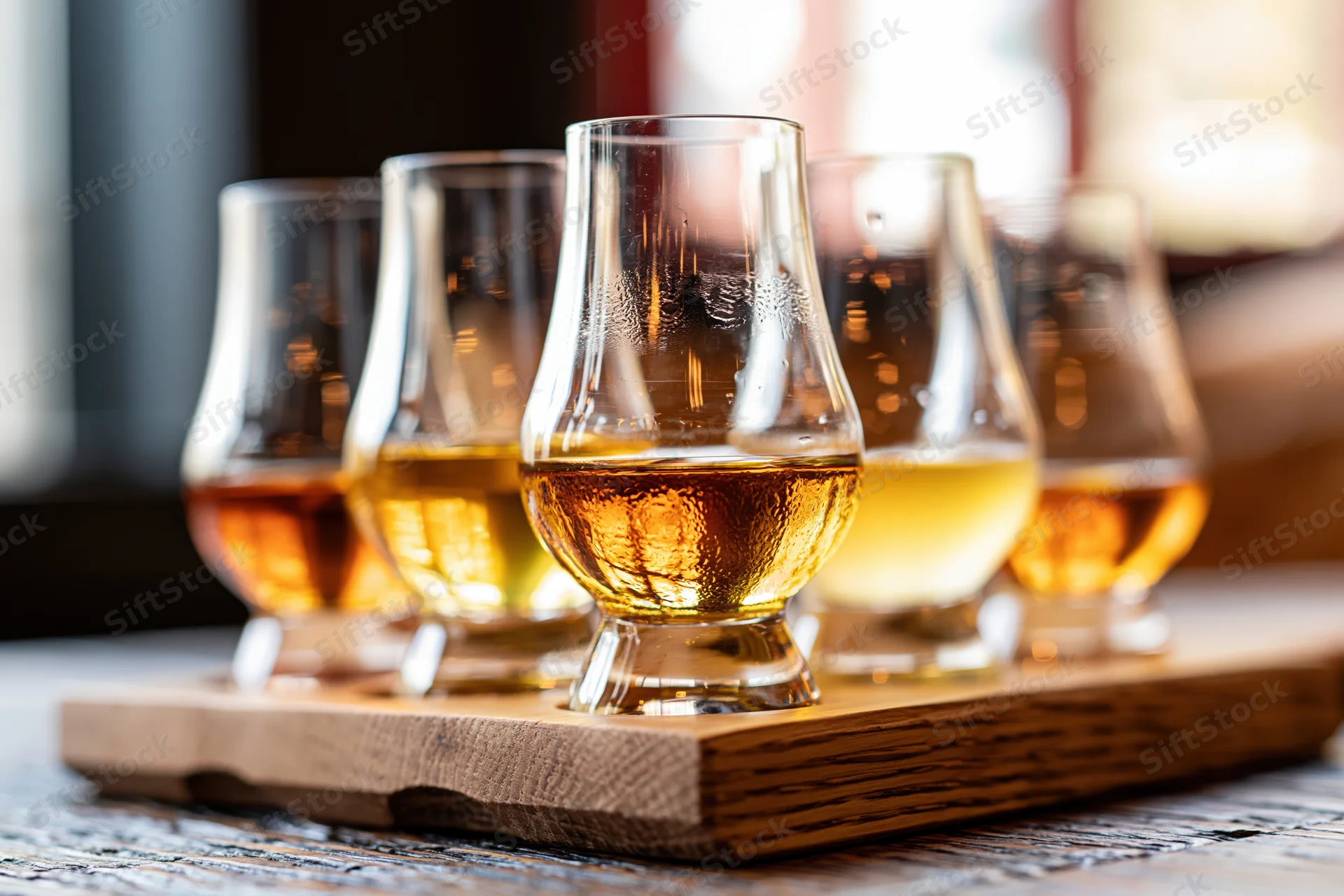 Five glencairn whisky glasses arranged in a wooden flight tray on a rustic tabletop
