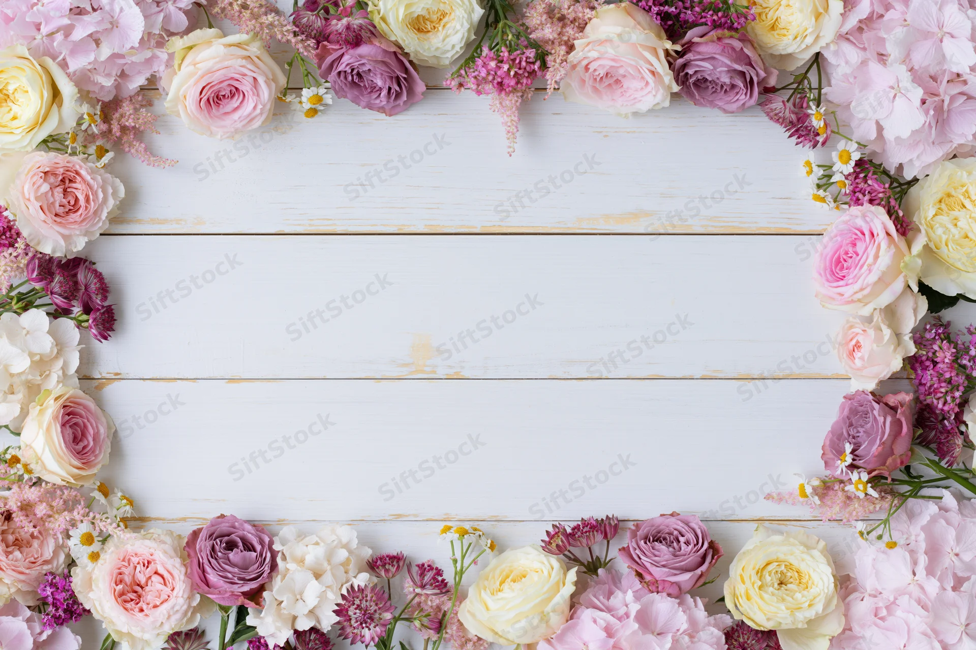 Mixed fresh flowers arranged in a loose border on a white wooden surface with copyspace in the center