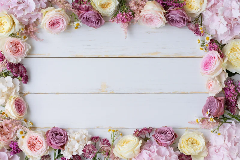 Mixed fresh flowers arranged in a loose border on a white wooden surface with copyspace in the center