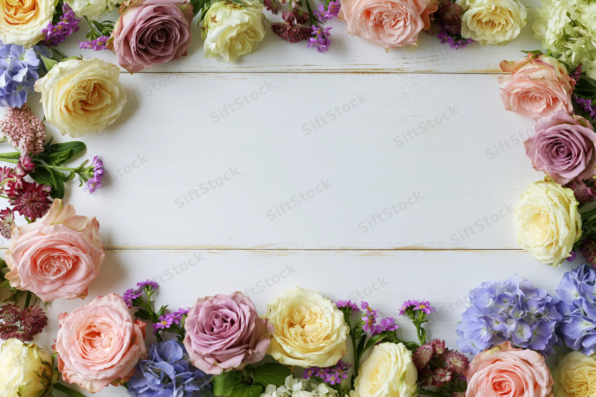 Mixed fresh flowers arranged in a loose border on a white wooden surface with copyspace in the center
