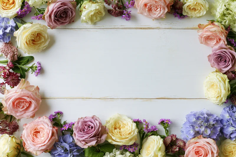 Mixed fresh flowers arranged in a loose border on a white wooden surface with copyspace in the center