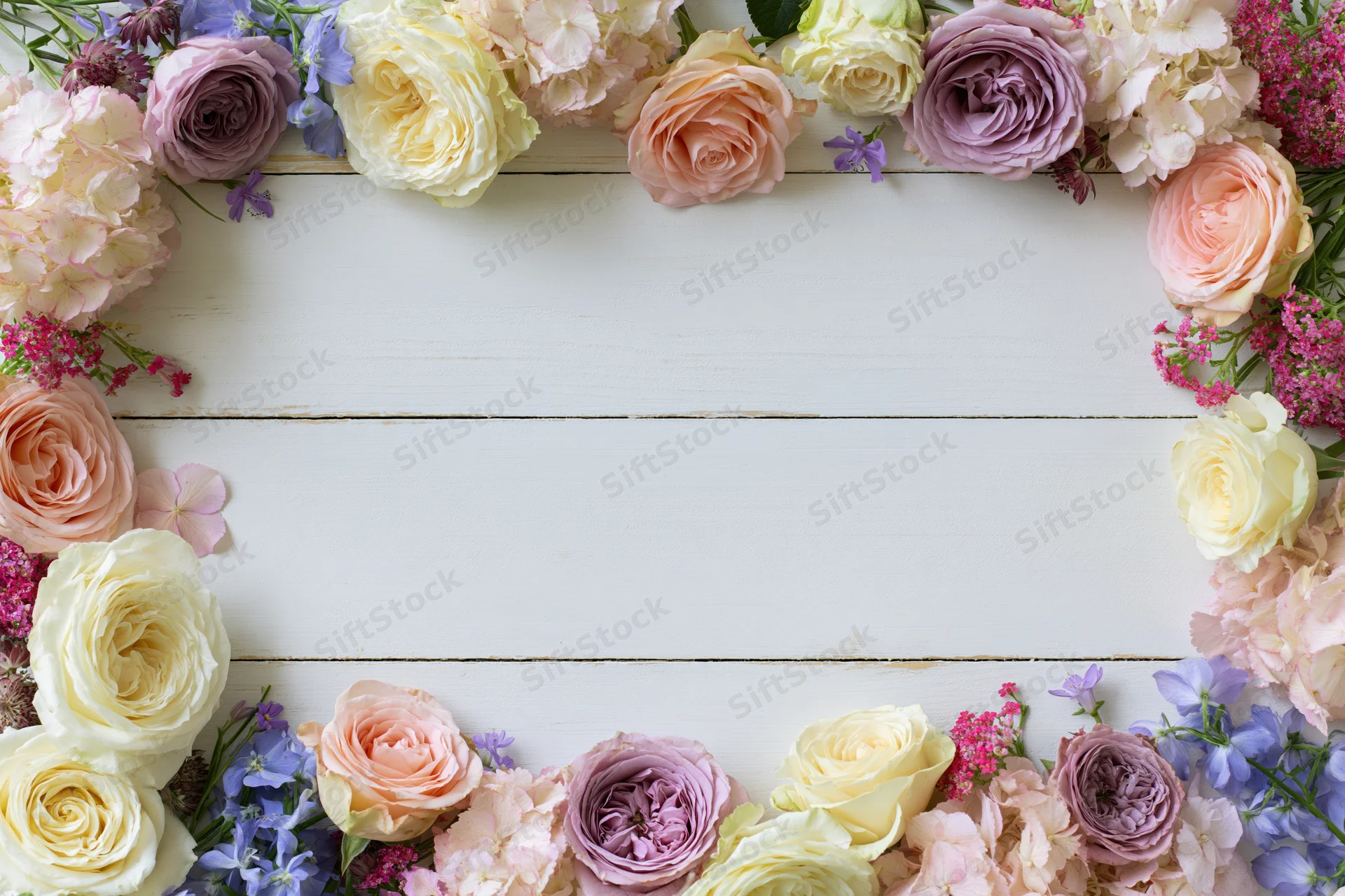 Mixed fresh flowers arranged in a loose border on a white wooden surface with copyspace in center