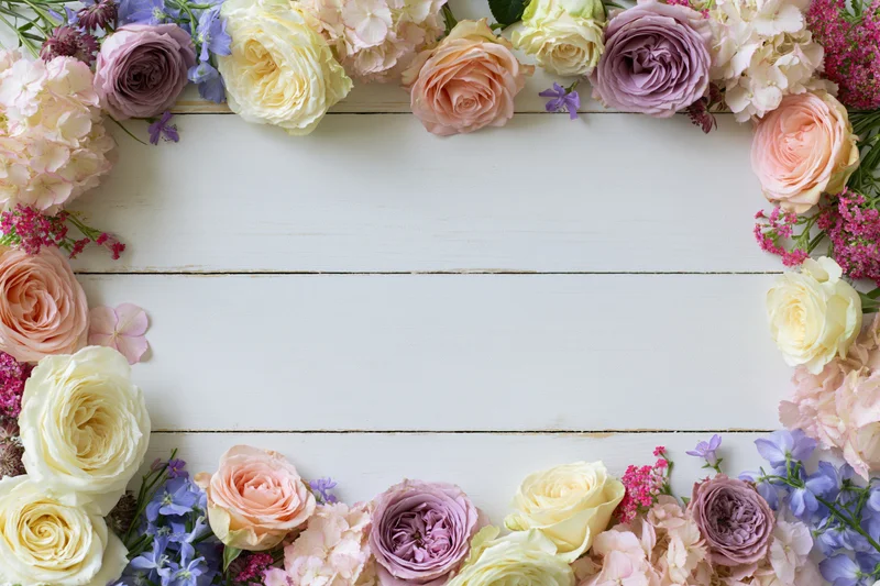 Mixed fresh flowers arranged in a loose border on a white wooden surface with copyspace in center