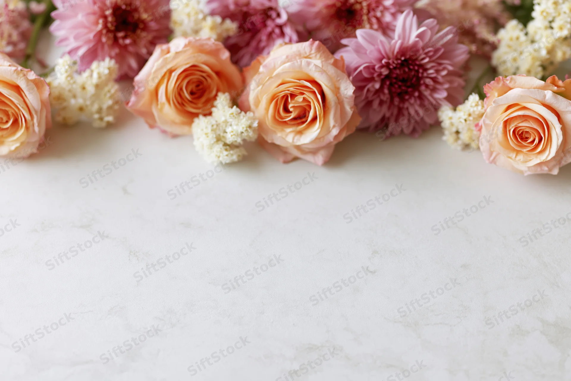 Flat lay of peach roses and pink chrysanthemums arranged on a white marble surface with copyspace