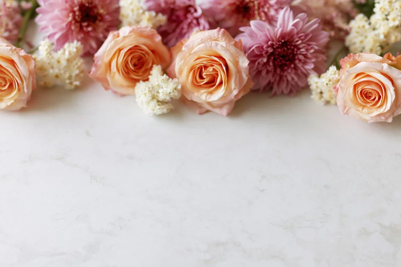 Flat lay of peach roses and pink chrysanthemums arranged on a white marble surface with copyspace