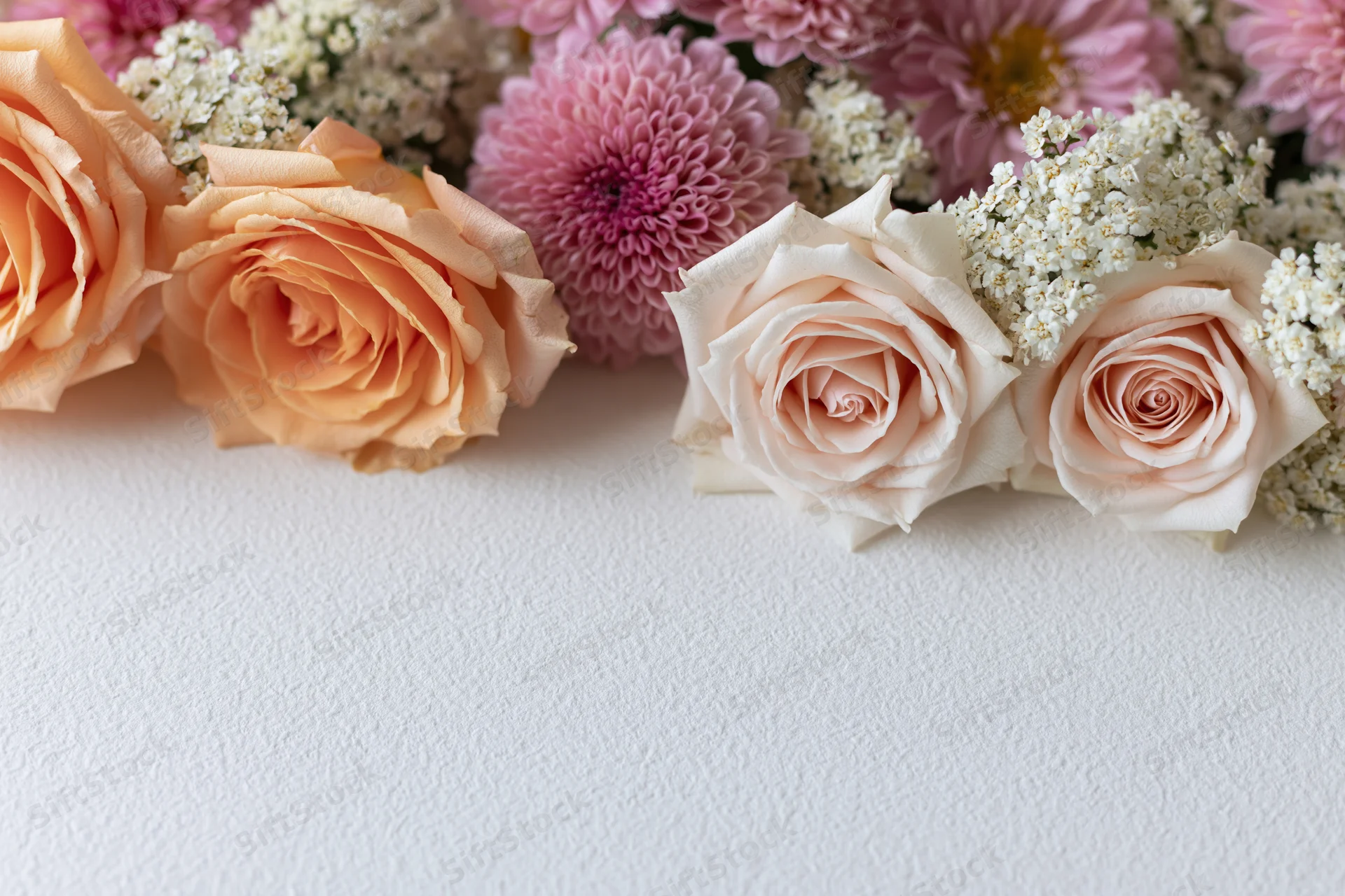 Flat lay of peach roses, pink chrysanthemums and white sprays arranged on textured white surface with copyspace