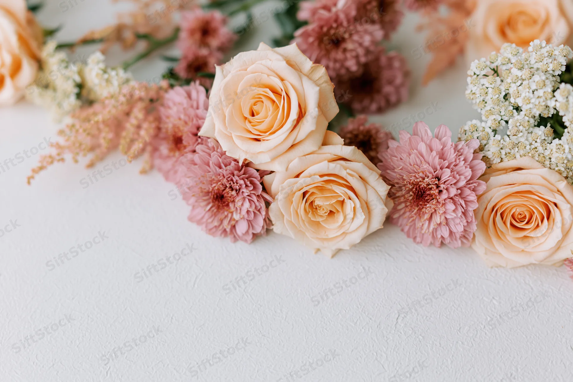 Flat lay floral arrangement of peach roses and pink chrysanthemums on white surface with copyspace