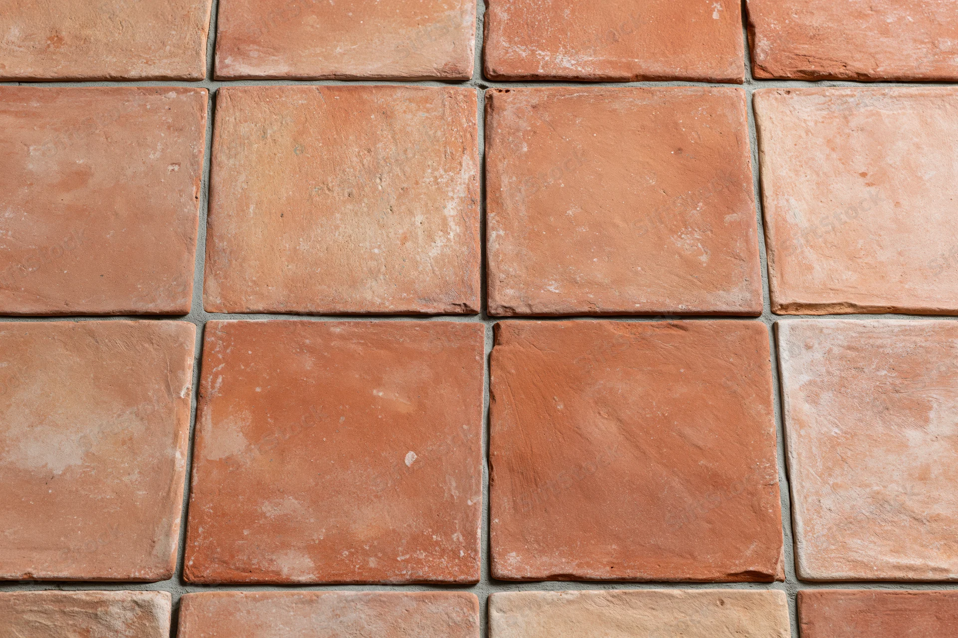 Aged terracotta floor tiles arranged in a grid pattern with visible grout lines