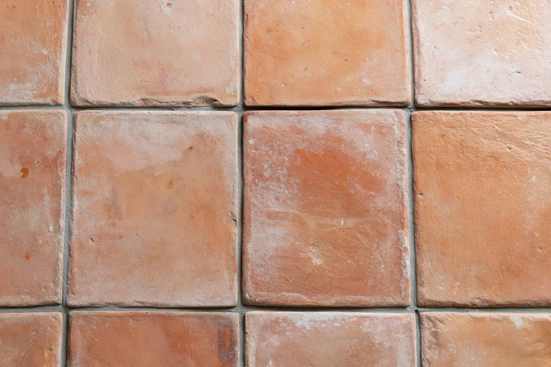 Aged terracotta floor tiles arranged in a grid pattern with visible grout lines and weathered texture