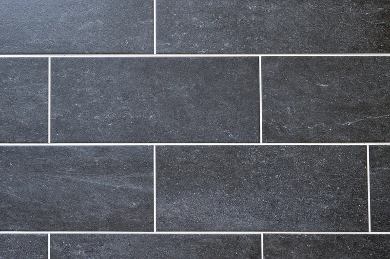 Dark charcoal ceramic floor tiles arranged in a brick pattern with white grout, close-up view